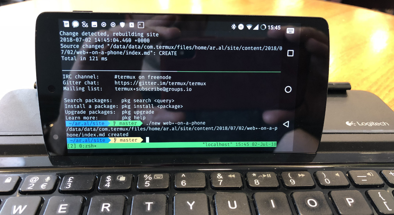 Photo of my Nexus 5 running LineageOS 14.1. On screen is a tmux terminal session in Termux showing a split screen between my blogs Hugo and rsync watchers running in one panel and a terminal prompt showing the result of a ./new web+-on-a-phone command that created a Markdown file for a blog post.